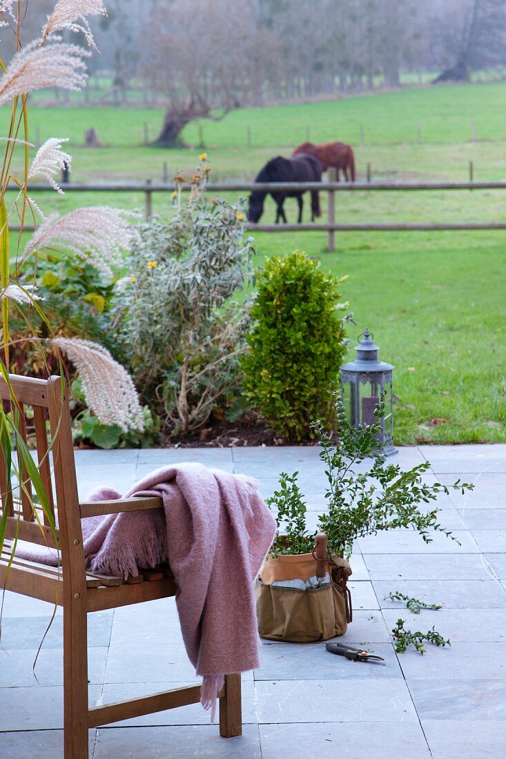 Holzbank mit Plaid und Pflanztopf auf Terrasse, Blick auf Pferdekoppel