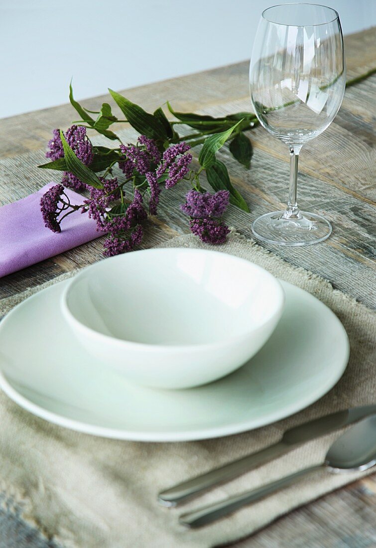 White place setting on linen place mat and sprig of flowers on rustic wooden table
