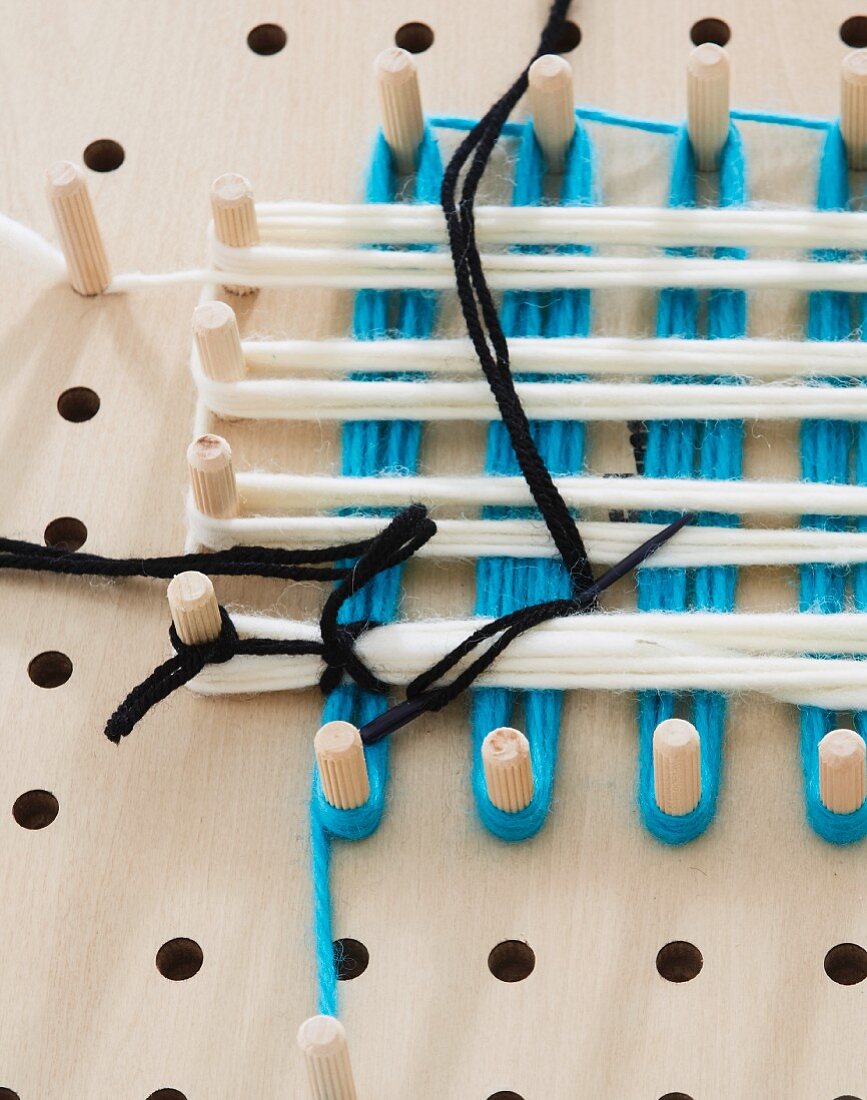 A pegboard with different coloured wool wrapped around the pegs