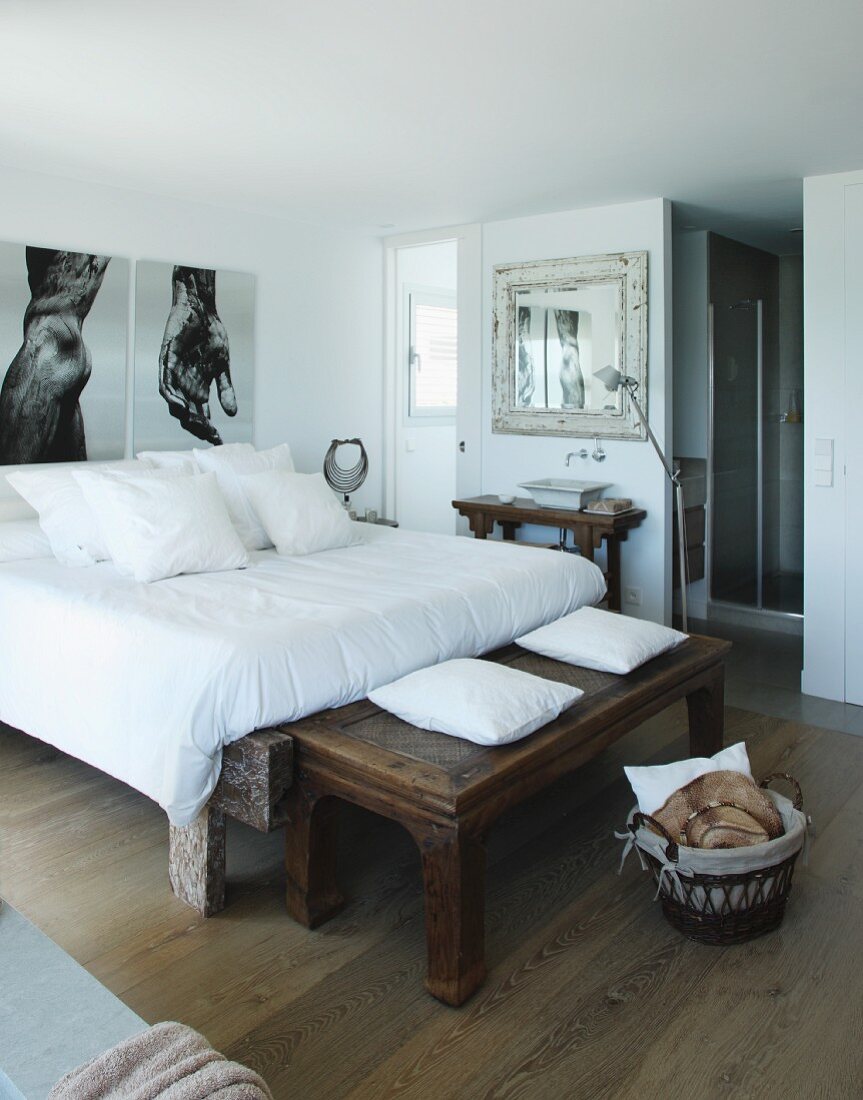 Rustikale Fussbank aus Holz am Doppelbett im Schlafzimmer, an Wand grossformatige Fotos