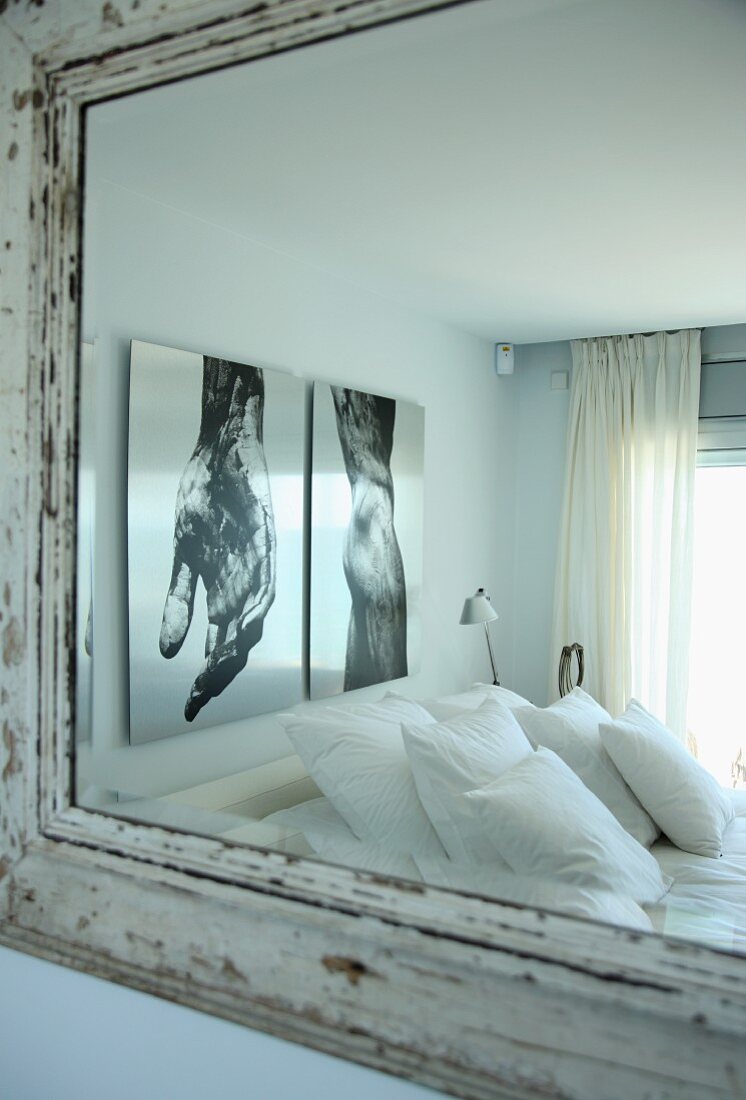 Kissenstapel auf Bett, vor Wand mit grossformatigen Fotos, in einem Wandspiegel reflektiert
