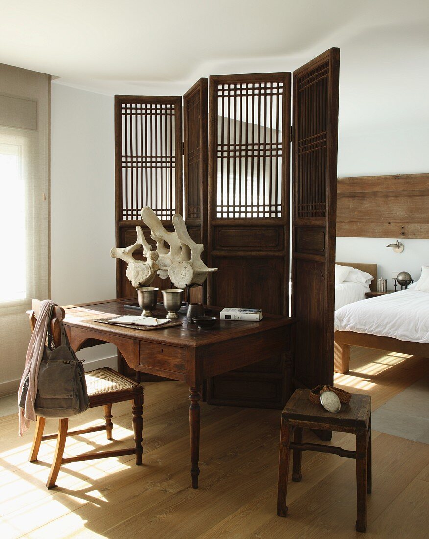 Antiker Sekretär und Stuhl vor Holz Paravent, dahinter Schlafplätze in schlichtem Raum mit gepflegtem Dielenboden