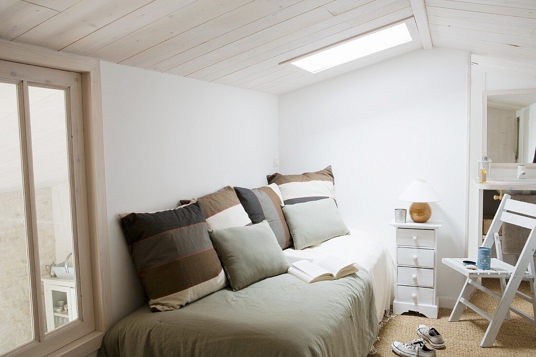 Kissen im Streifenlook auf Bett in schlichtem Zimmer unter Oberlicht in Decke