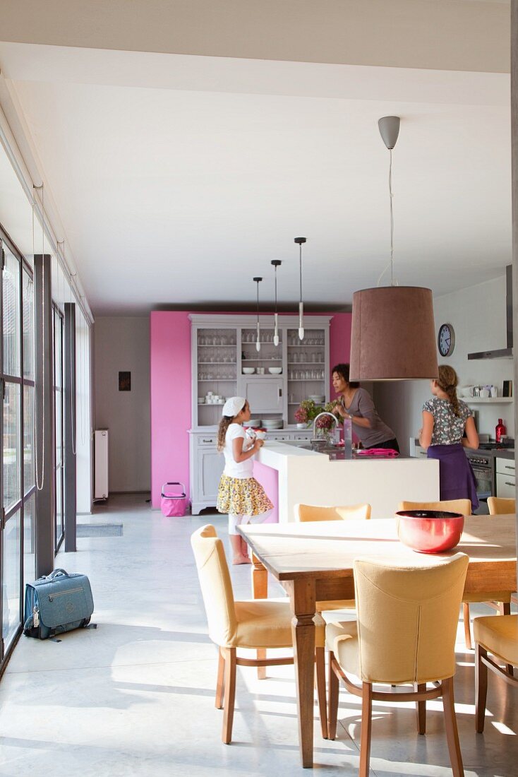 Offene Küche mit moderner Küchentheke, pinkfarbener Raumteilerwand und gemütlichem Essbereich, im Hintergrund Frau mit zwei Mädchen