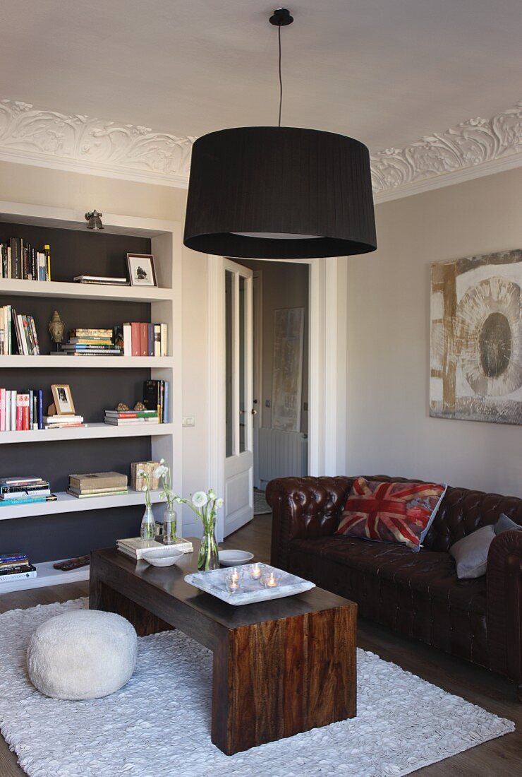 Pendant lamp with black lampshade above seating area with retro leather sofa and coffee table made of solid, exotic wood