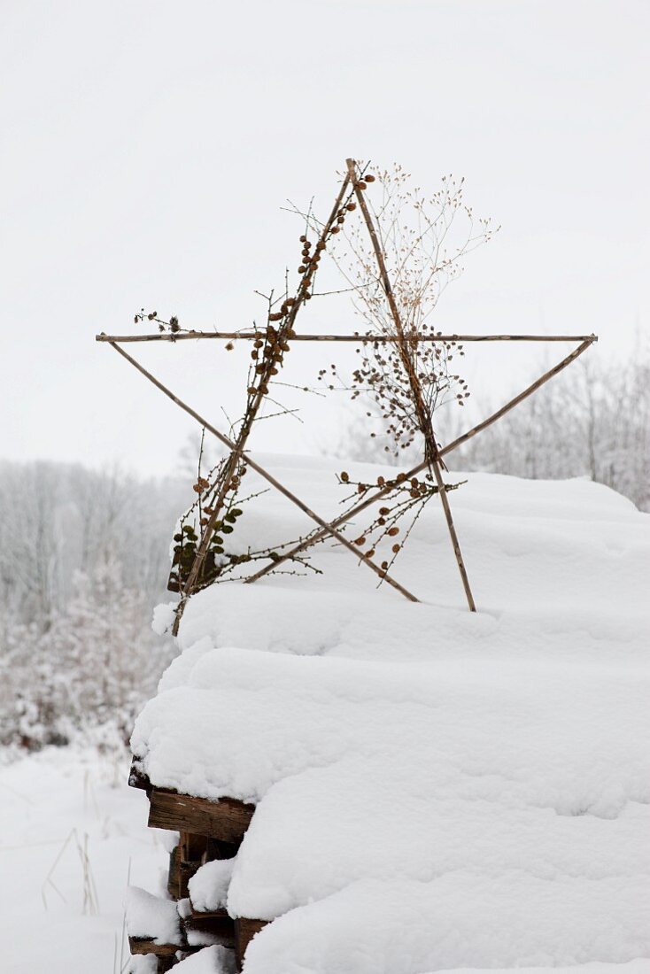 Dekostern aus Holzstäben auf schneebedecktem Brennholzstapel