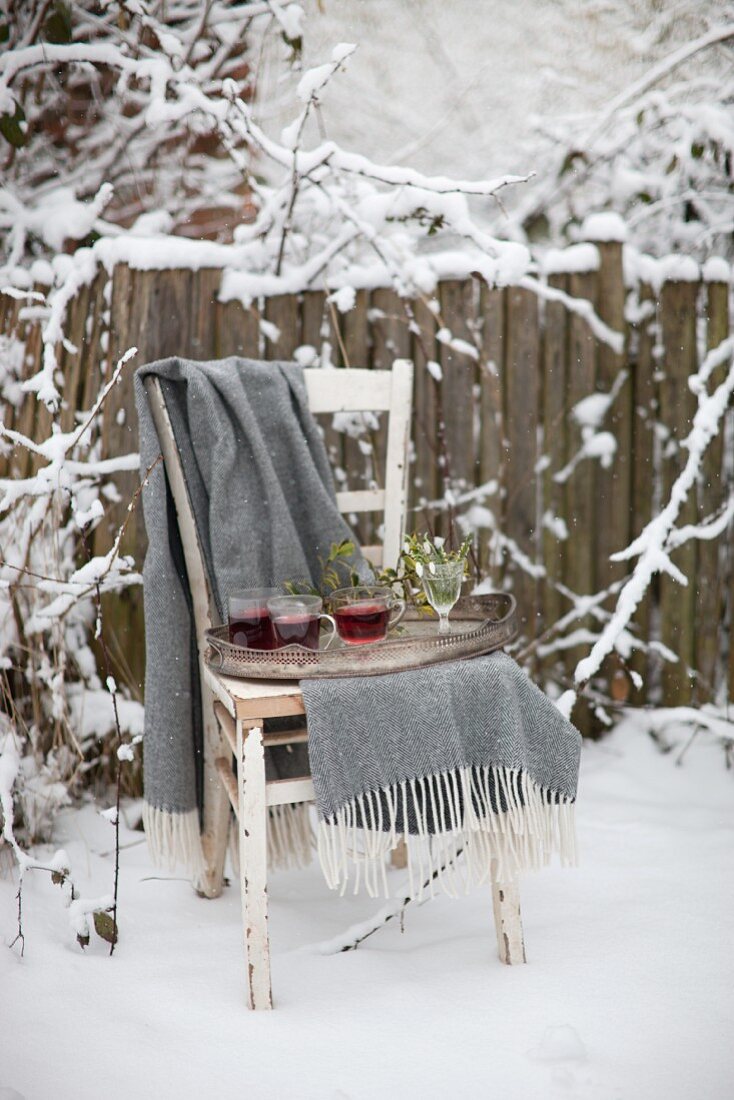 Tray of mulled wine and blanket on old wooden chair in snowy garden
