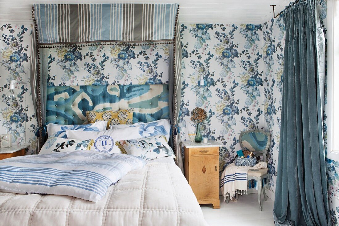 Doppelbett mit gepolstem Kopfteil unter blaugrau gestreiftem Baldachin in Schlafzimmer mit blauer Blumentapete