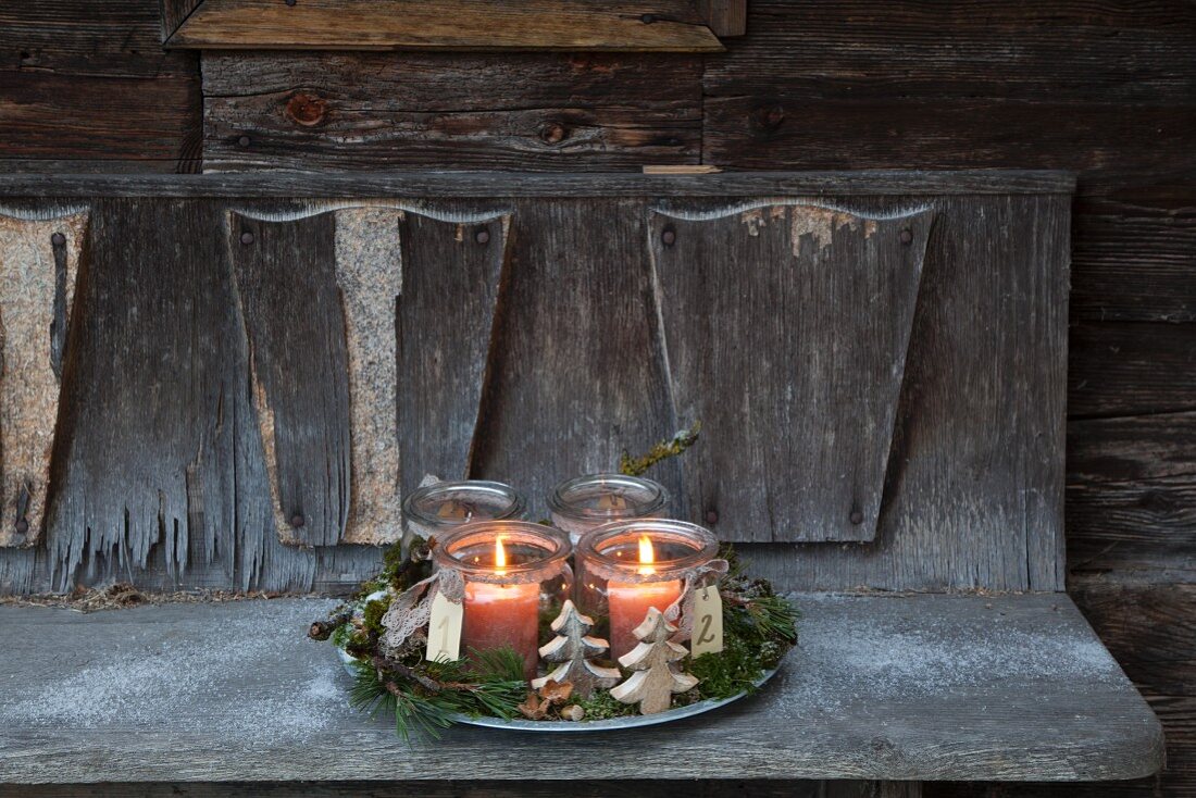 with two lit candles in mason jars on weathered wooden bench
