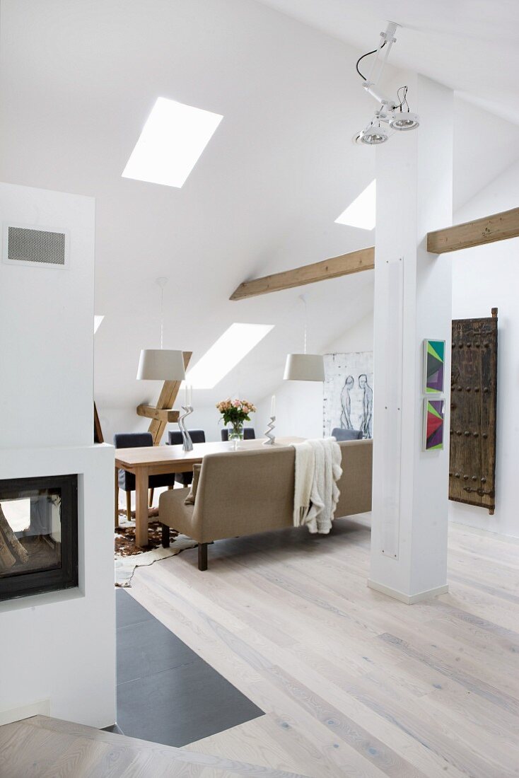 Converted, open-plan attic with pale wooden floor, dining area with table and upholstered bench