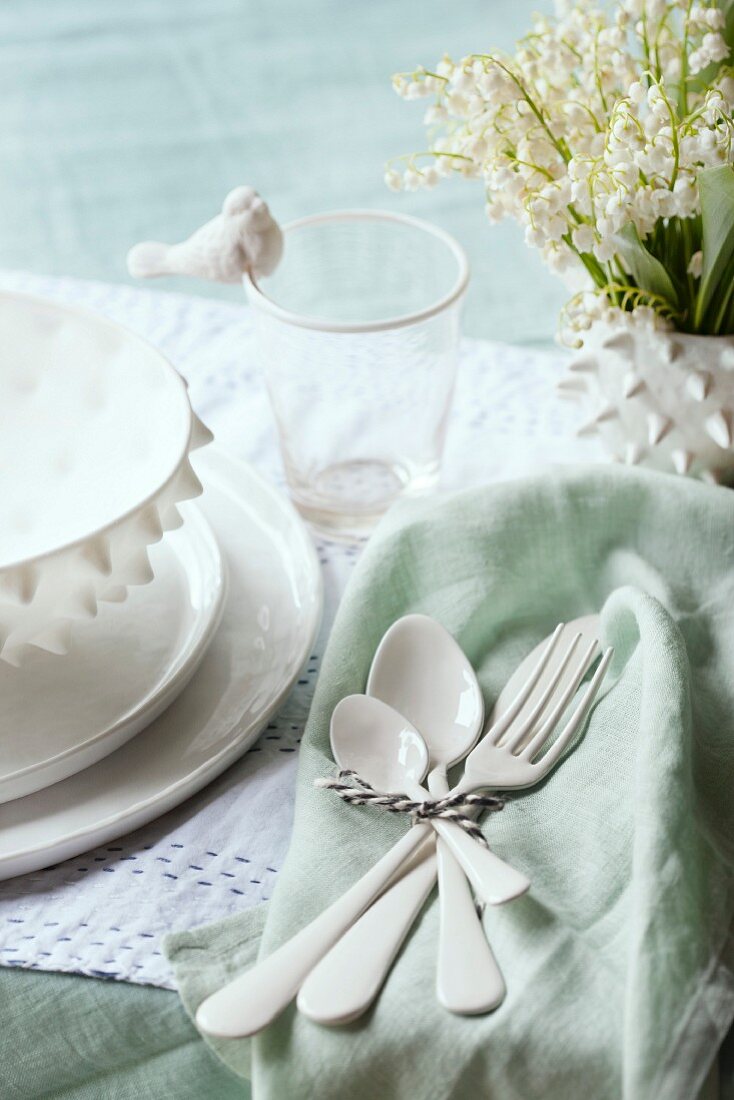 White ceramic cutlery on pastel green napkin next to place setting