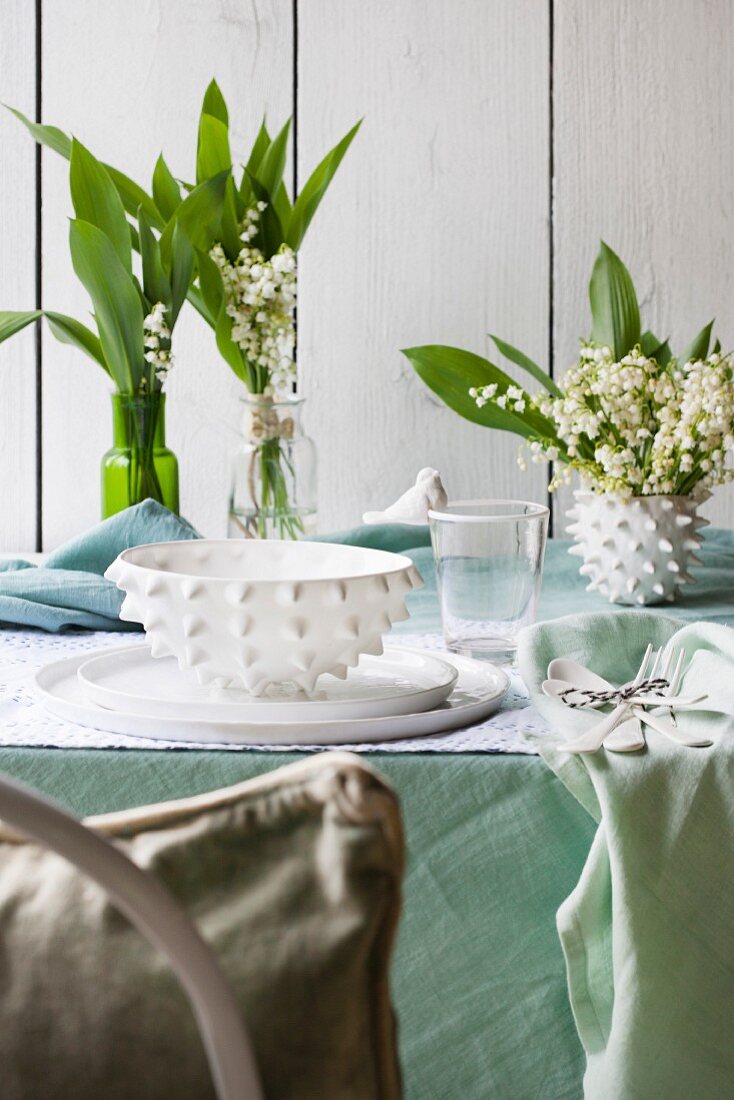 Weisses Gedeck und Maiglöckchen auf Tisch mit pastellgrüner Tischdecke im Freien