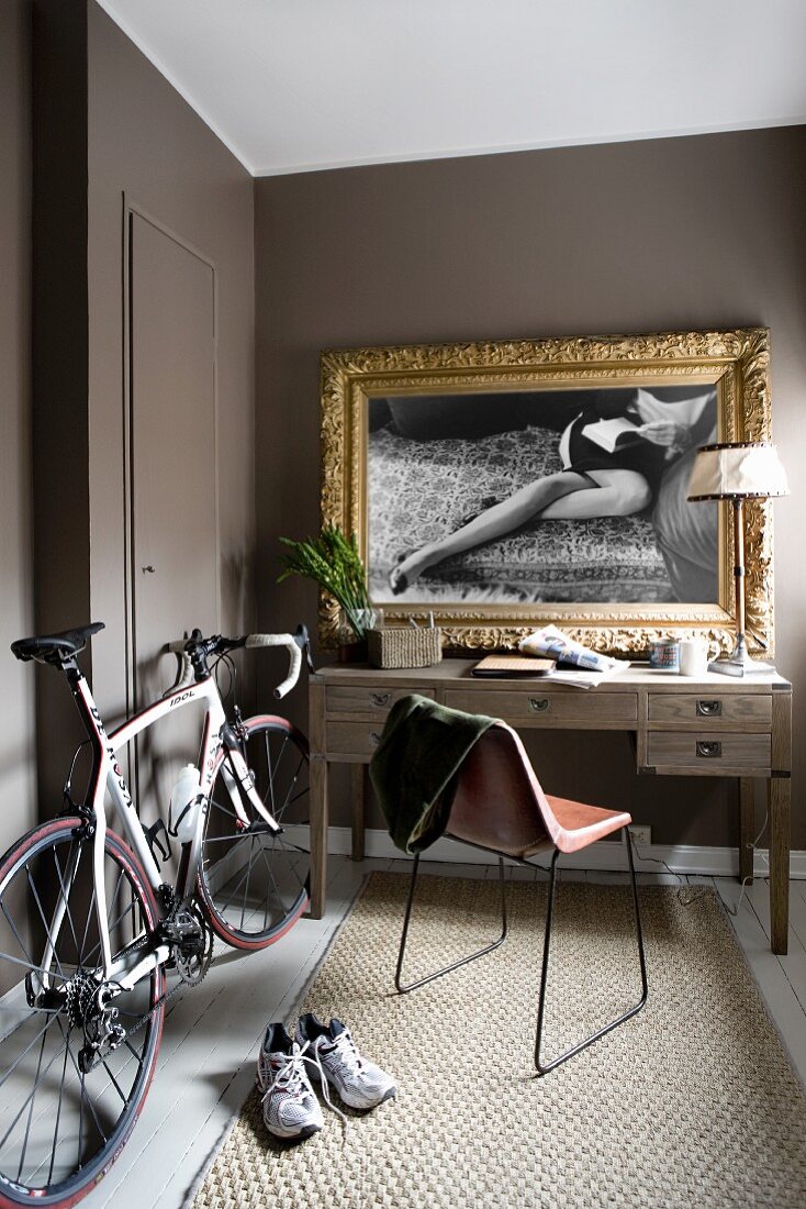 Rennrad neben Schreibtisch, an Wand schwarz-weiss Foto mit Goldrahmen
