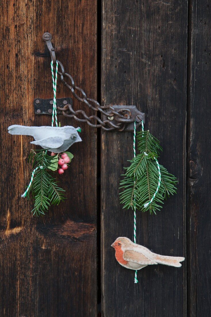 Selbstgebastelte Vogelanhänger aus Wollfilz mit Tannenzweigen am Kettenschloss eines Vintage-Holztores