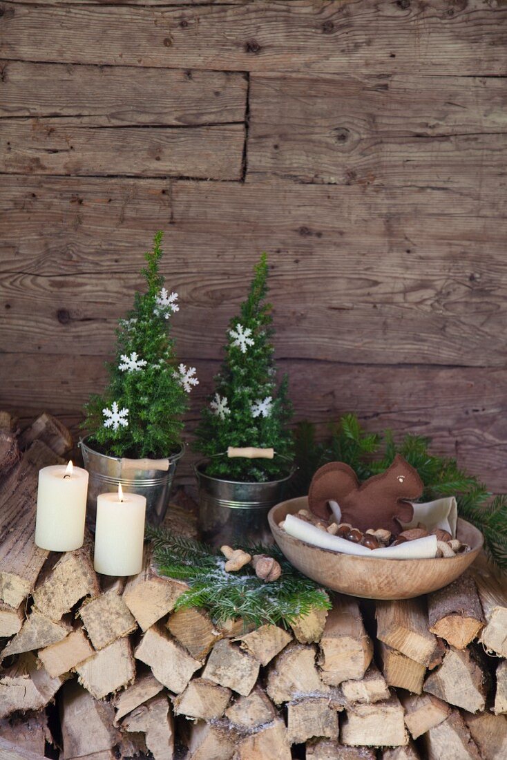 DIY-Eichhörnchen aus Filz in Holzschale mit Nüssen auf weihnachtlich dekoriertem Brennholzstapel an Hüttenwand