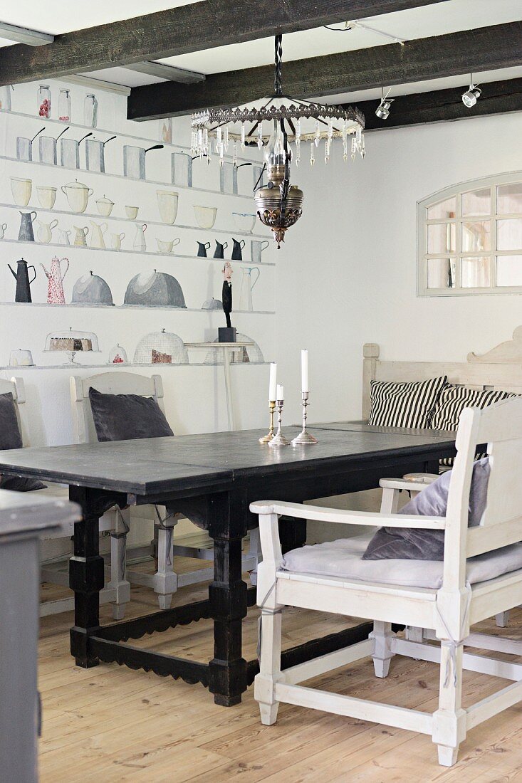 White-painted armchairs around table with carved base frame in rustic dining room with mural on wall