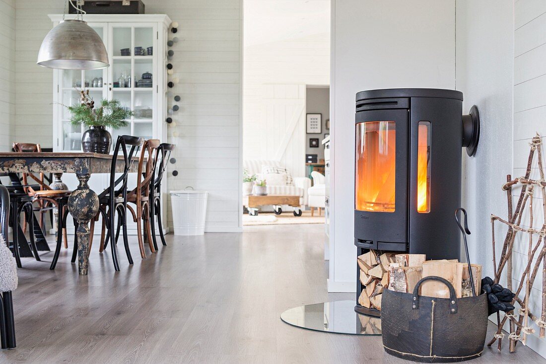Cast iron log burner with firewood compartment and dining area in open-plan interior with white wood cladding