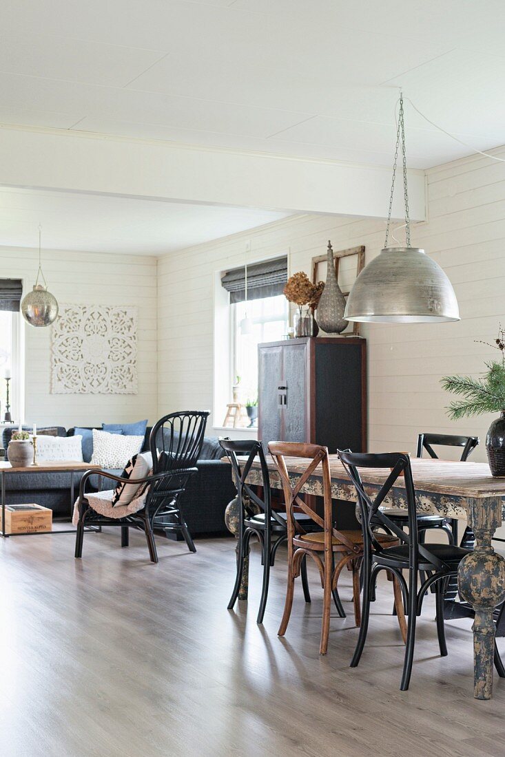 Bugholzstühle um Esstisch unter Pendelleuchte mit Metallschirm, im Hintergrund gemütliche Couchecke in offenem Wohnraum mit weisser Holzverkleidung