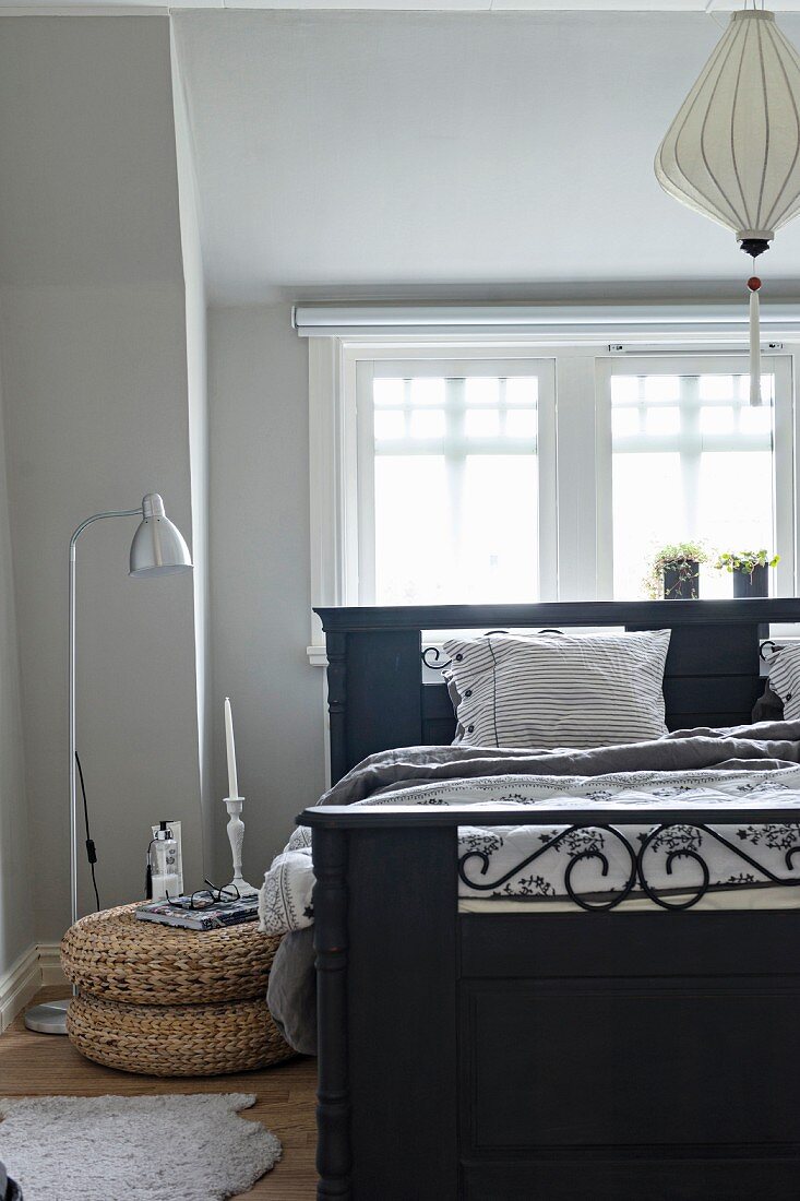 Antique, black-painted wooden bed and standard lamp with stainless steel lampshade below window in bedroom painted pale grey