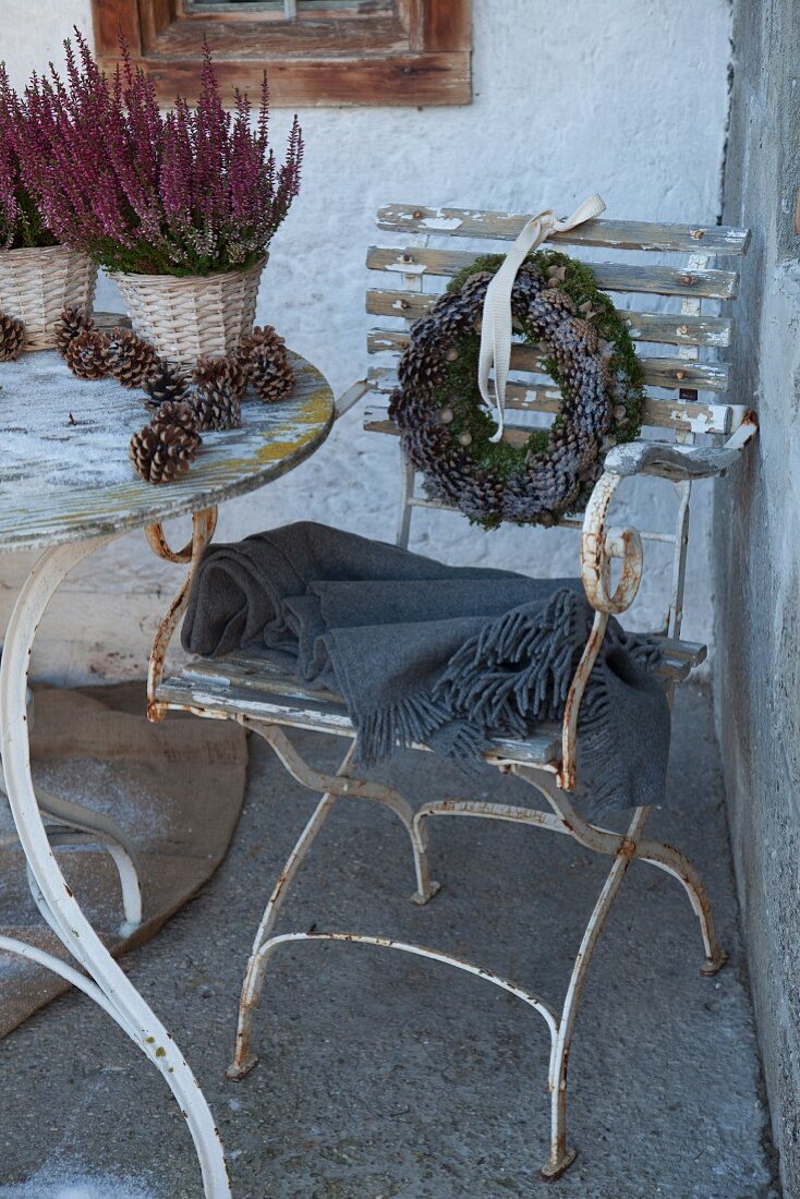 Vintage Gartenstuhl mit abgeblätterter Farbe und grauem Plaid, an Rückenlehne aufgehängter Kranz mit Tannenzapfen