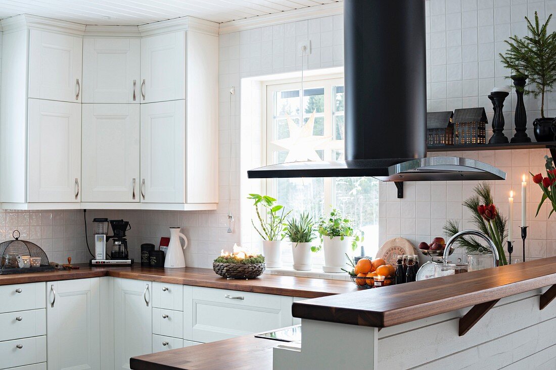 weiße Küche mit Holzarbeitsplatten, Dunstabzug hinter Frühstückstheke