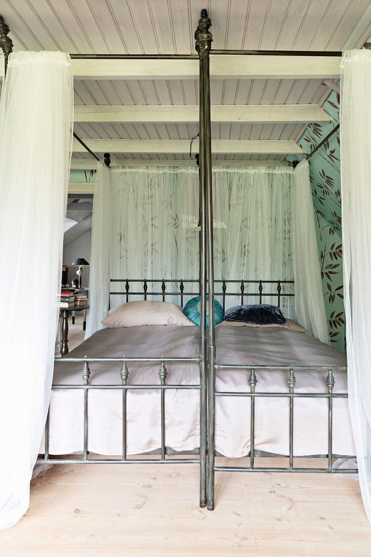 Vintage four-poster bed with airy curtains on metal frame