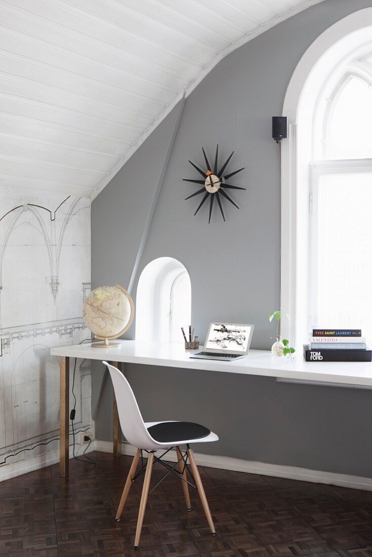 Klassikerstuhl mit weisser Sitzschale vor Arbeitstisch am Fenster, grau getönte Wand, im Dachzimmer mit Tonnendecke