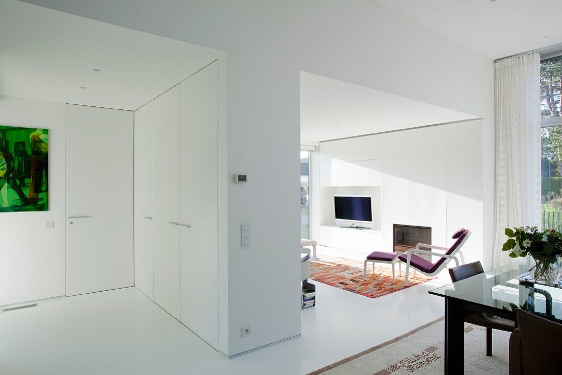 Modern, white open-plan interior with fitted cupboards in partition screening lounge area