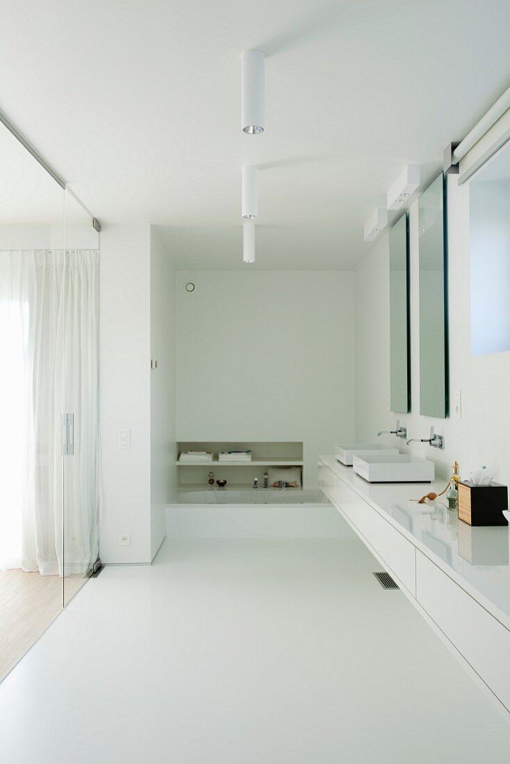 Long, minimalist floating washstand with white base unit mounted between two walls in white bathroom