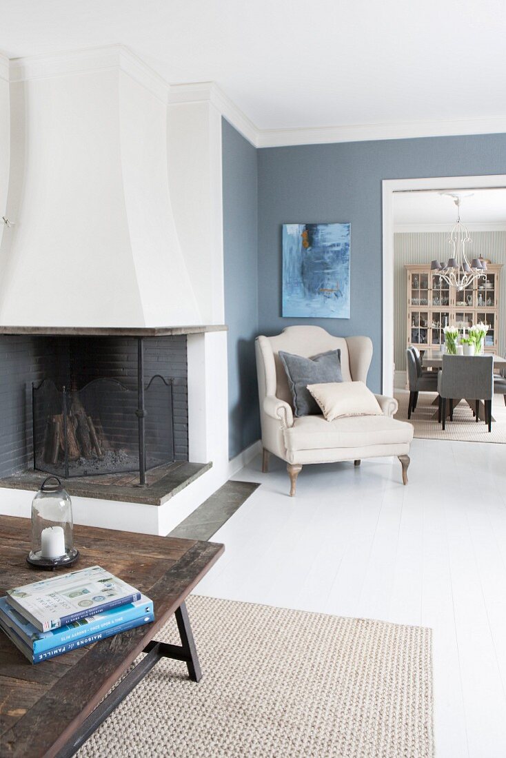 Offener Wohnbereich mit Kamin und elegantem Armlehnsessel vor taubenblauer Zimmerecke