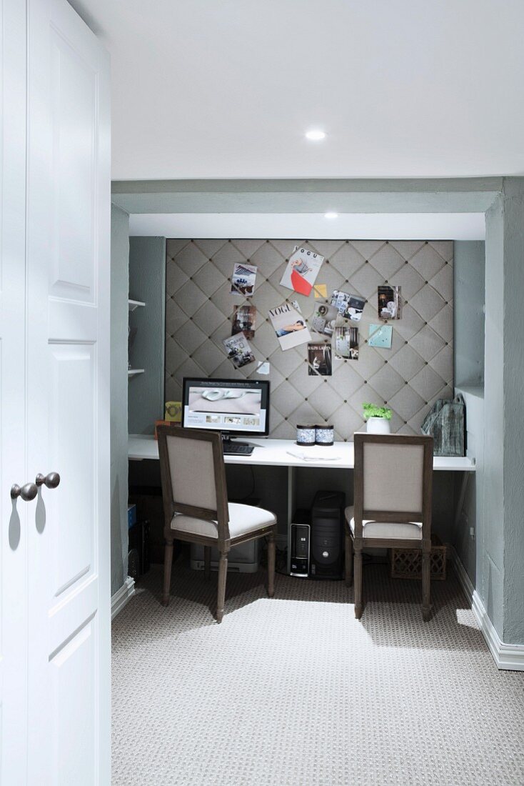 Home Office mit Schreibtisch und Computerbildschirm vor eleganter, gepolsterter Pinnwand