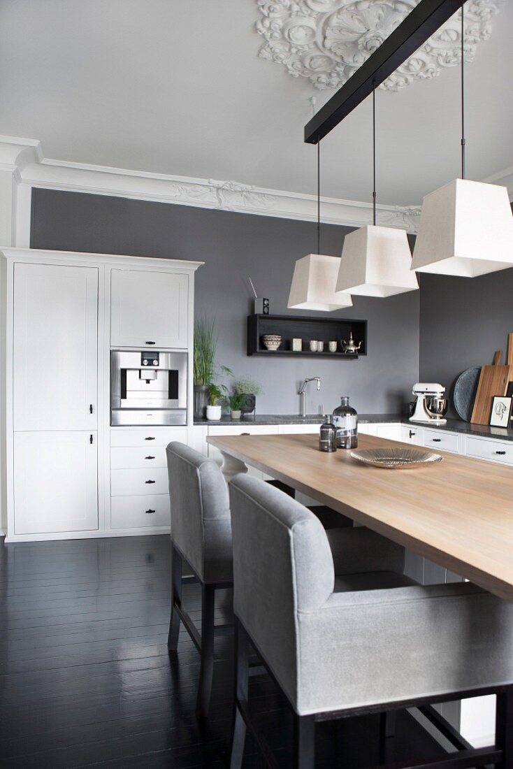 Upholstered chairs with pale grey covers at wooden table below three pendant lamps in kitchen-dining room