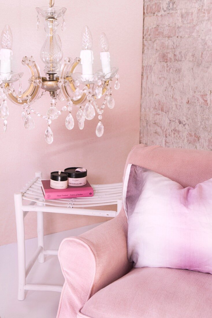 Rosa Polstersessel mit Kissen und Beistelltisch unter Kristall-Kronleuchter vor rosa getönter Wand