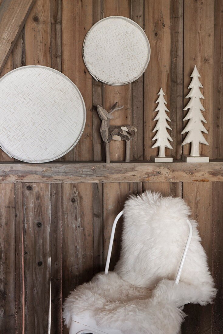 Stuhl mit weißem Schaffell vor rustikaler Holzwand mit Weihnachtsdeko