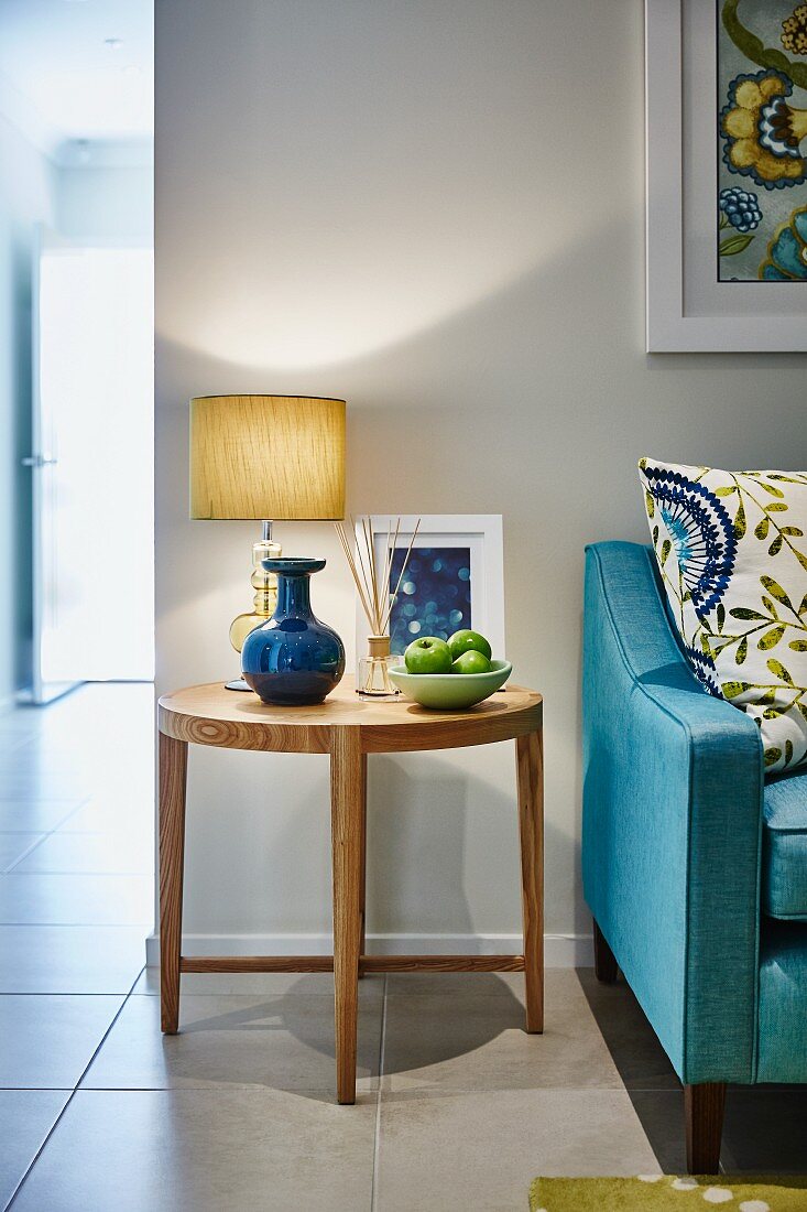 Obstschale und Tischleuchte auf rundem Beistelltisch aus Holz neben hellblauer Couch