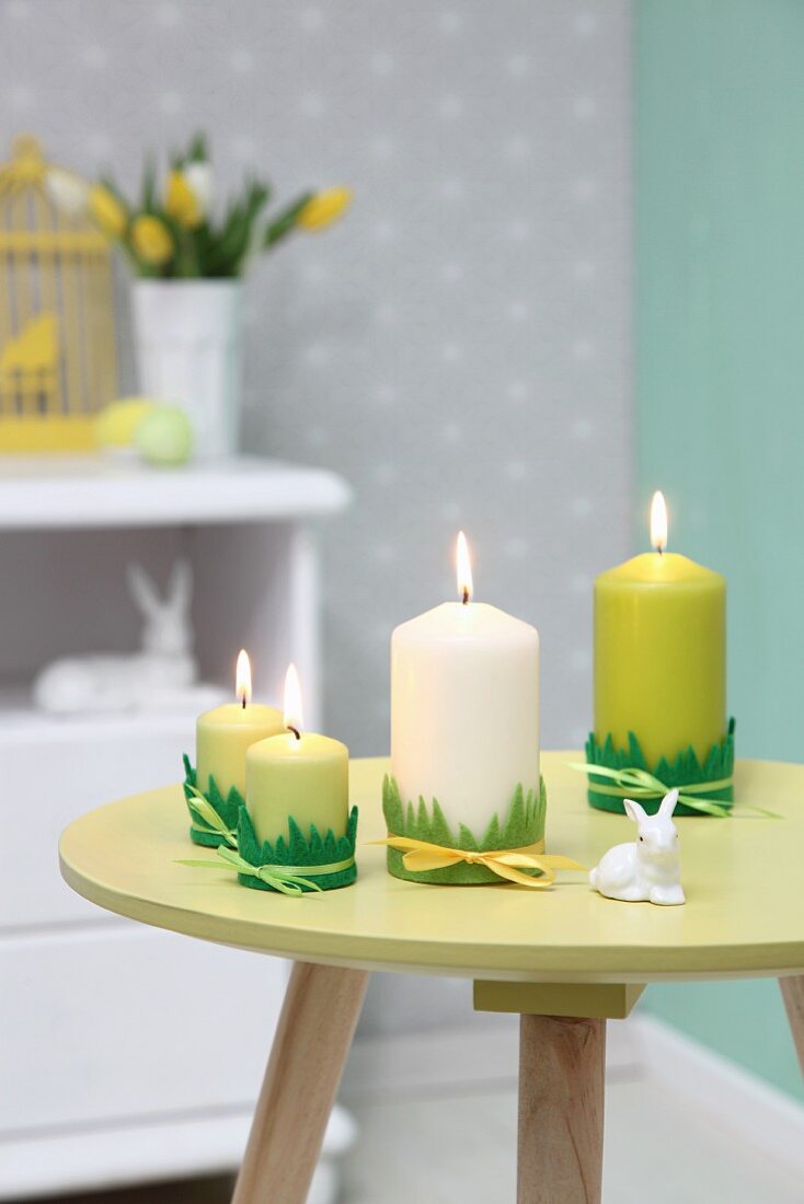 Osterdeko in Grüntönen: Kerzen mit Grasdeko und Hasenfigur auf rundem Tischchen
