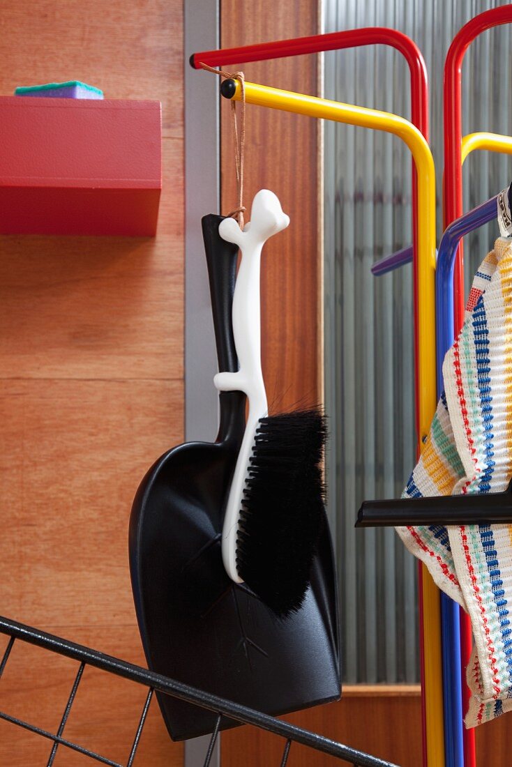 Brush with animal-shaped handle and black dustpan hanging from colourful, retro coat rack