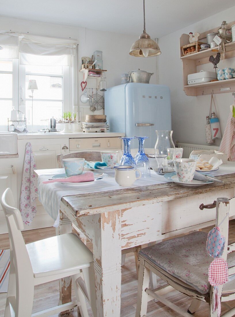 Esstisch mit Stühlen in nostalgischer Shabby Wohnküche, im Hintergrund blauer Kühlschrank