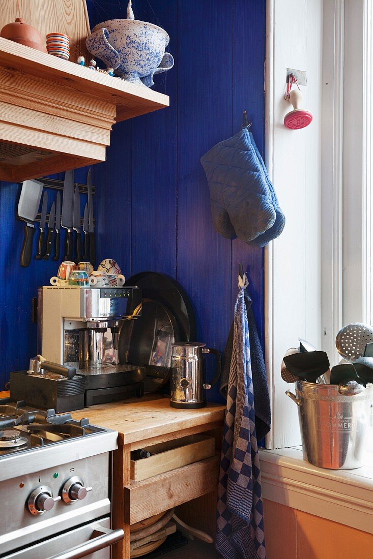 Blue-painted wooden wall and coffee machine on solid wooden base units in corner of kitchen