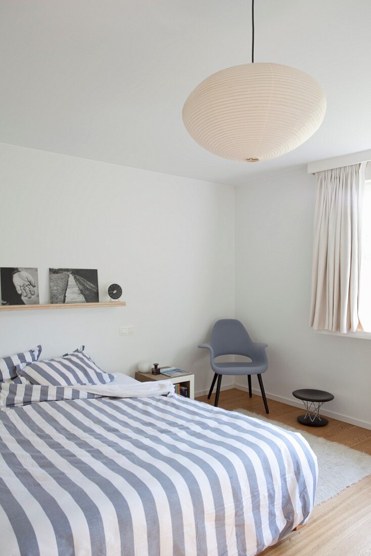 Doppelbett mit gestreifter Bettwäsche, seitlich Retro Stuhl in modernem Schlafzimmer, Pendelleuchte mit Papierschirm