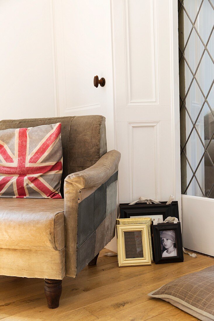 Union flag cushion on old leather armchair next to picture frame leaning against door frame