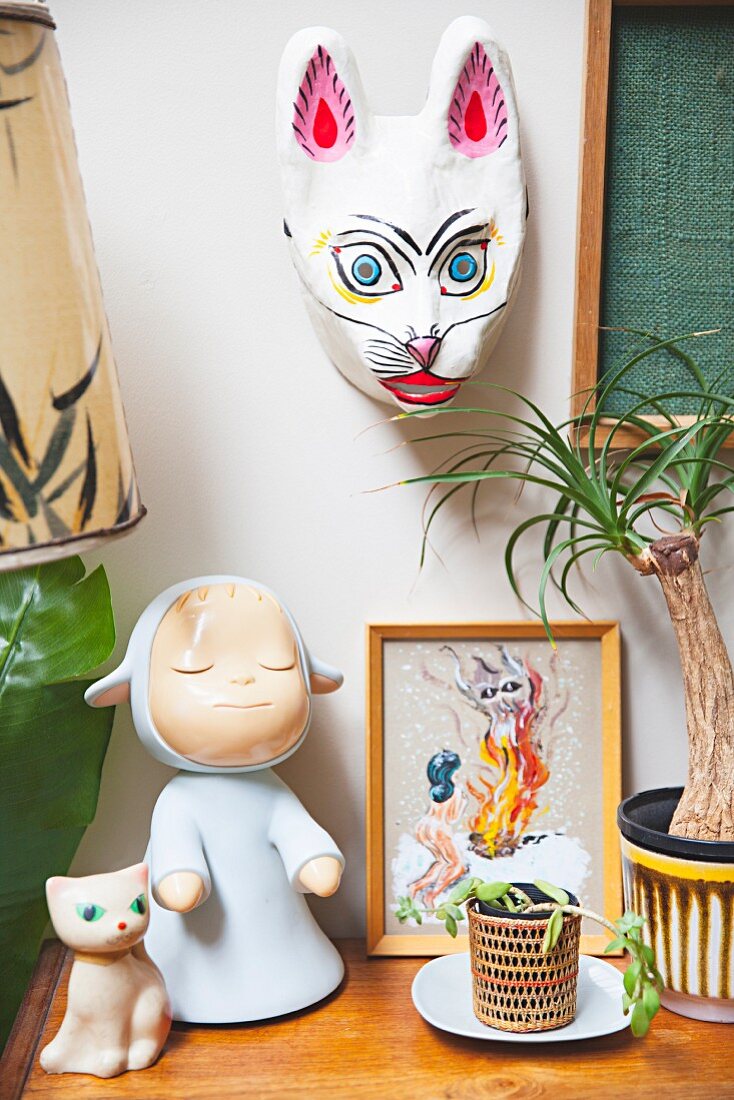 Retro Spielsachen, Puppe und Katzenfigur neben Zimmerpflanze, an Wand Tiermaske