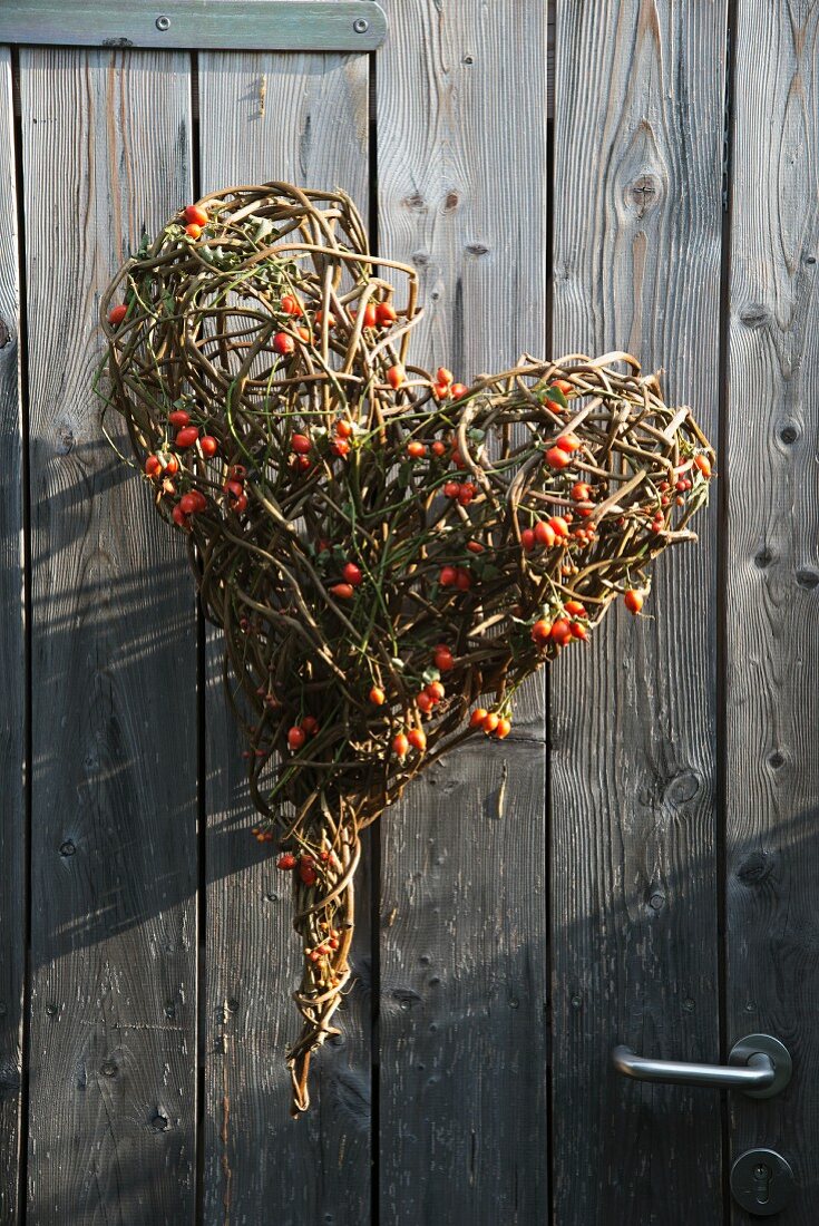 Herzform aus Zweigen und Hagebuttenfrüchten an Holztür aufgehängt