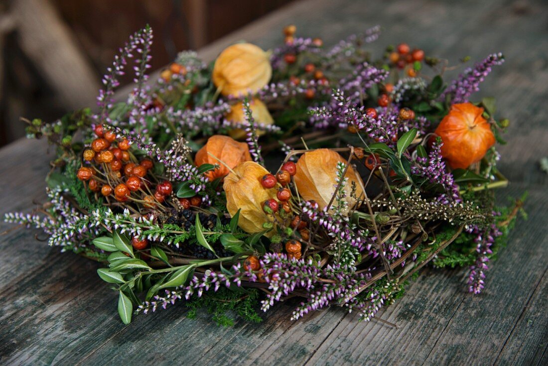Wreath of physalis, heather and sprigs of berries on wooden surface
