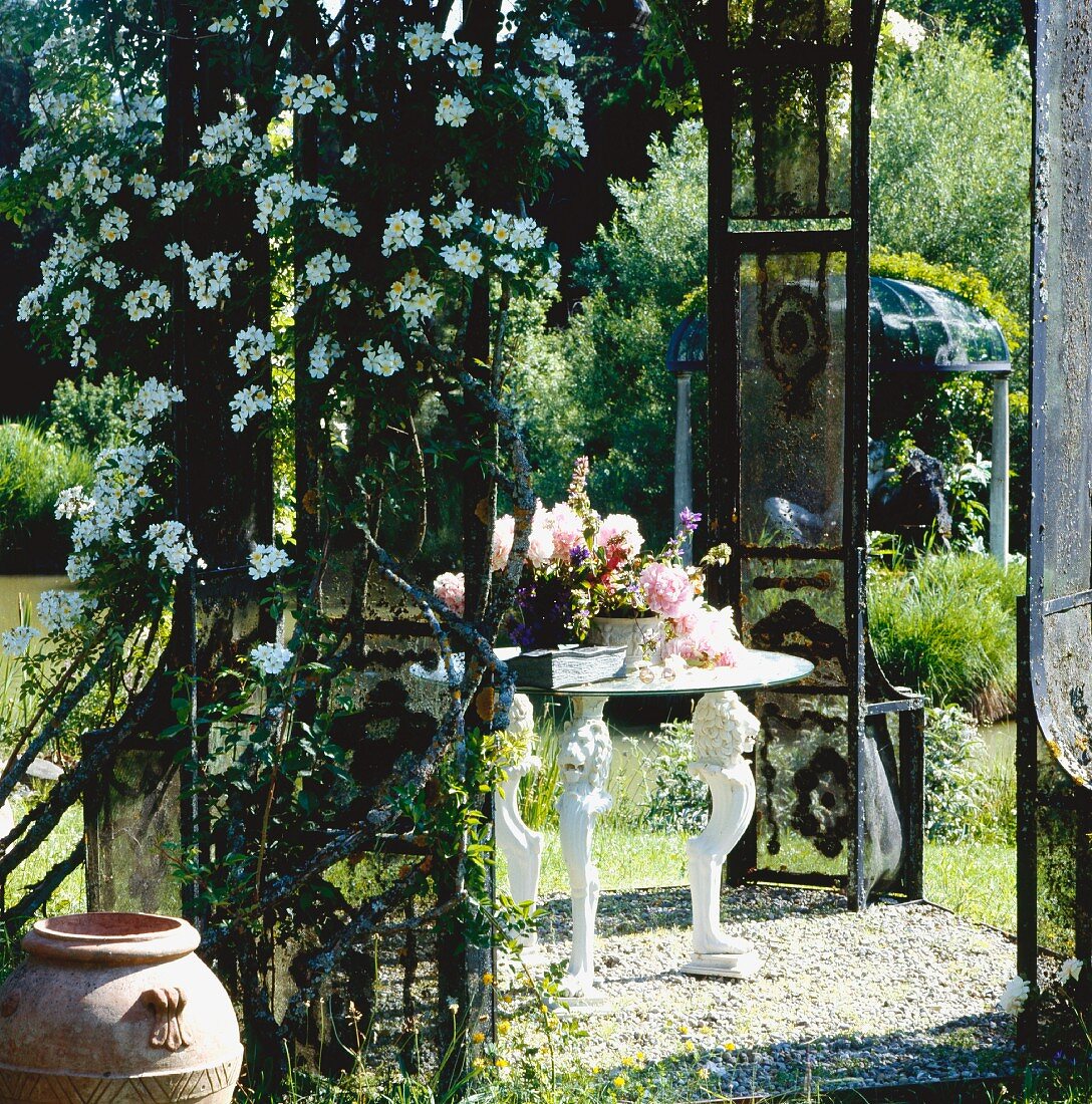 Blumentöpfe auf weißem Tisch mit Löwenfüssen in sonnigem Gartenpavillon mit Kletterpflanze