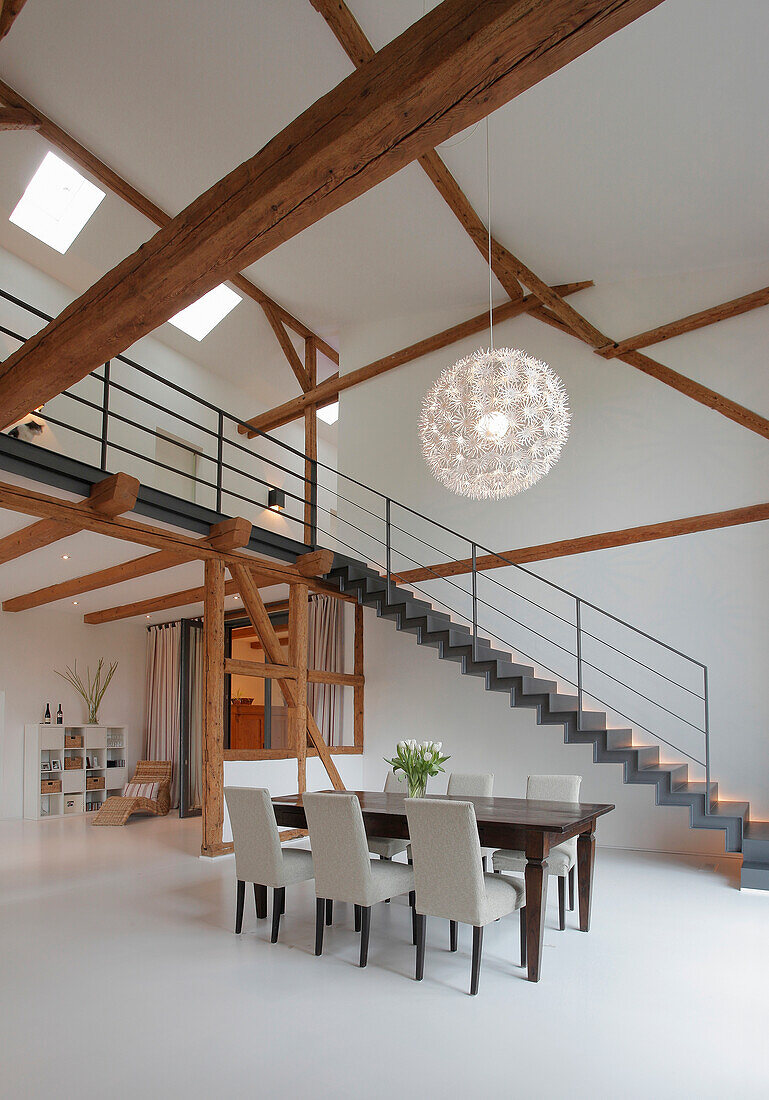 Essbereich in hellem Loft mit freiliegenden Holzbalken, Treppe und Hängeleuchte