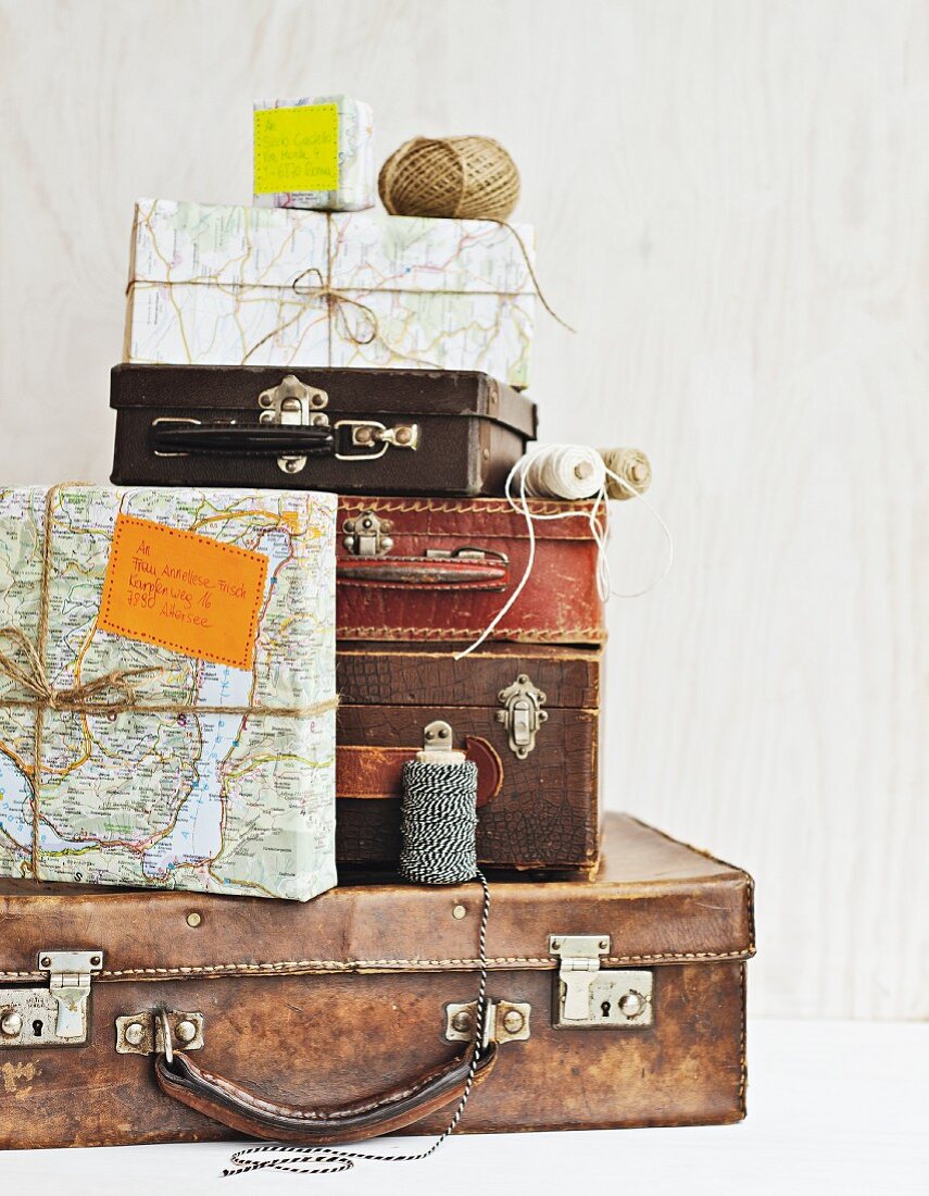 Verschiedengrosse Vintage-Koffer und Pakete mit Geschenkpapier aus Landkarten eingewickelt
