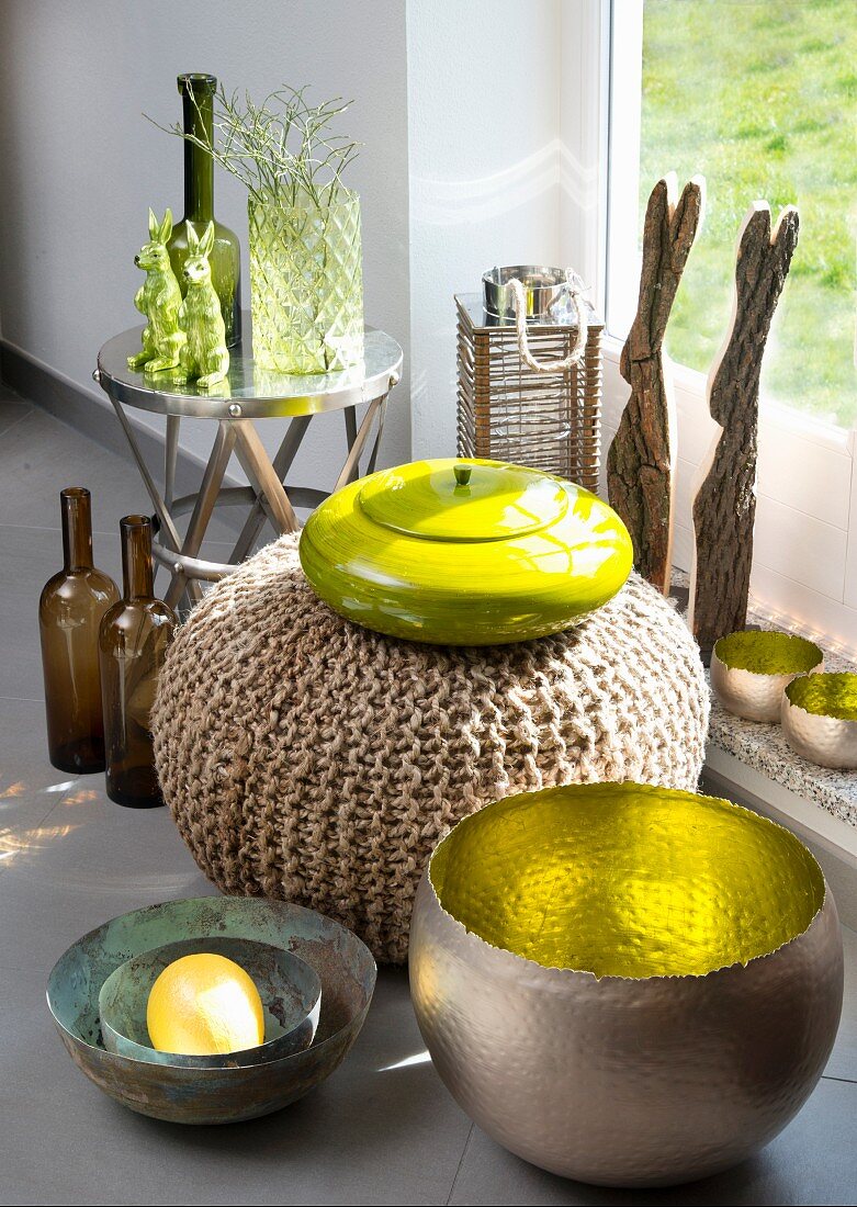 Verschiedene Behälter im Materialmix, Metallschale mit vergoldeter Innenseite vor Sitzpouf und gelbe Keramikdose mit Deckel