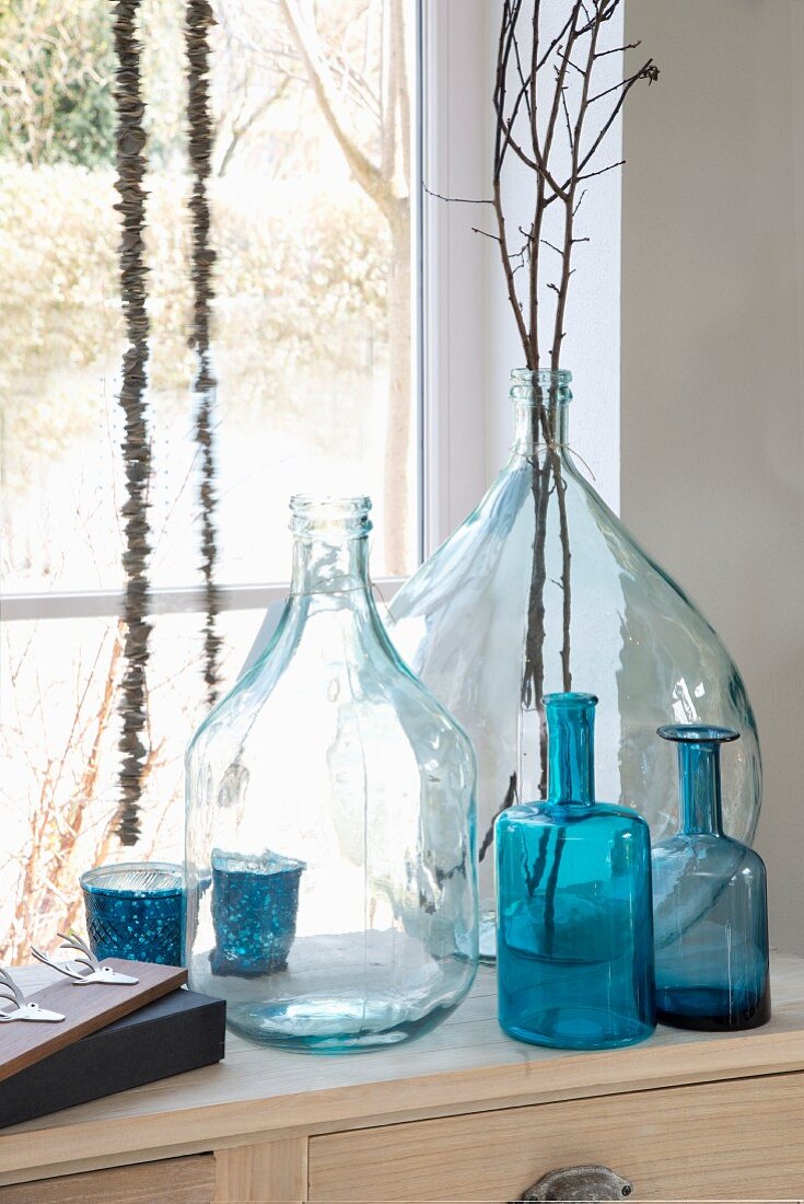 Various clear and blue glass bottles and twigs in front of window