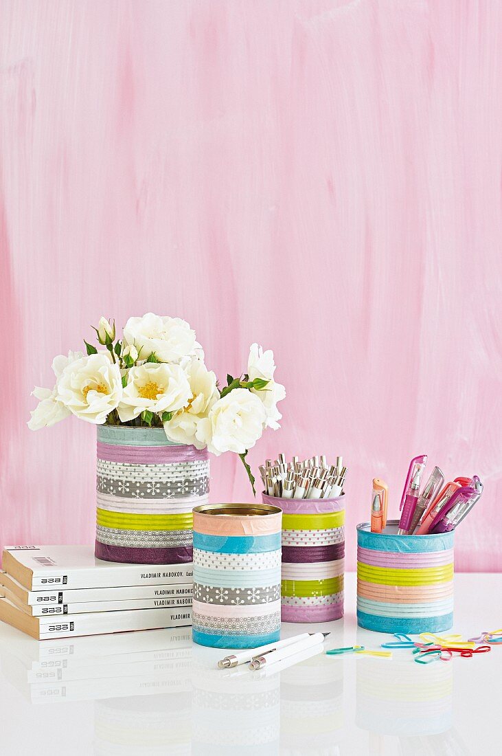Tins covered with washi tape used as pen holders and vases against pink background